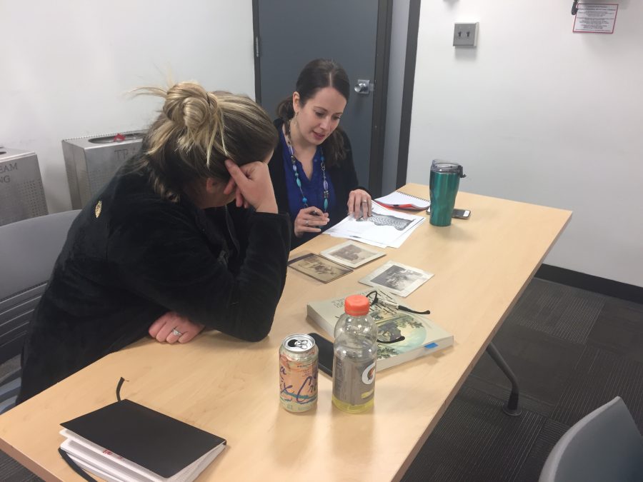 This is a photograph of two students in a classroom looking at and talking about historic photographs together.
