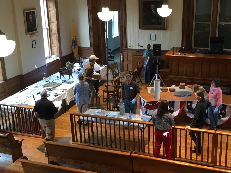 This is a photograph of four people cleaning artifacts inside a historic courtroom. Photo take from balcony.